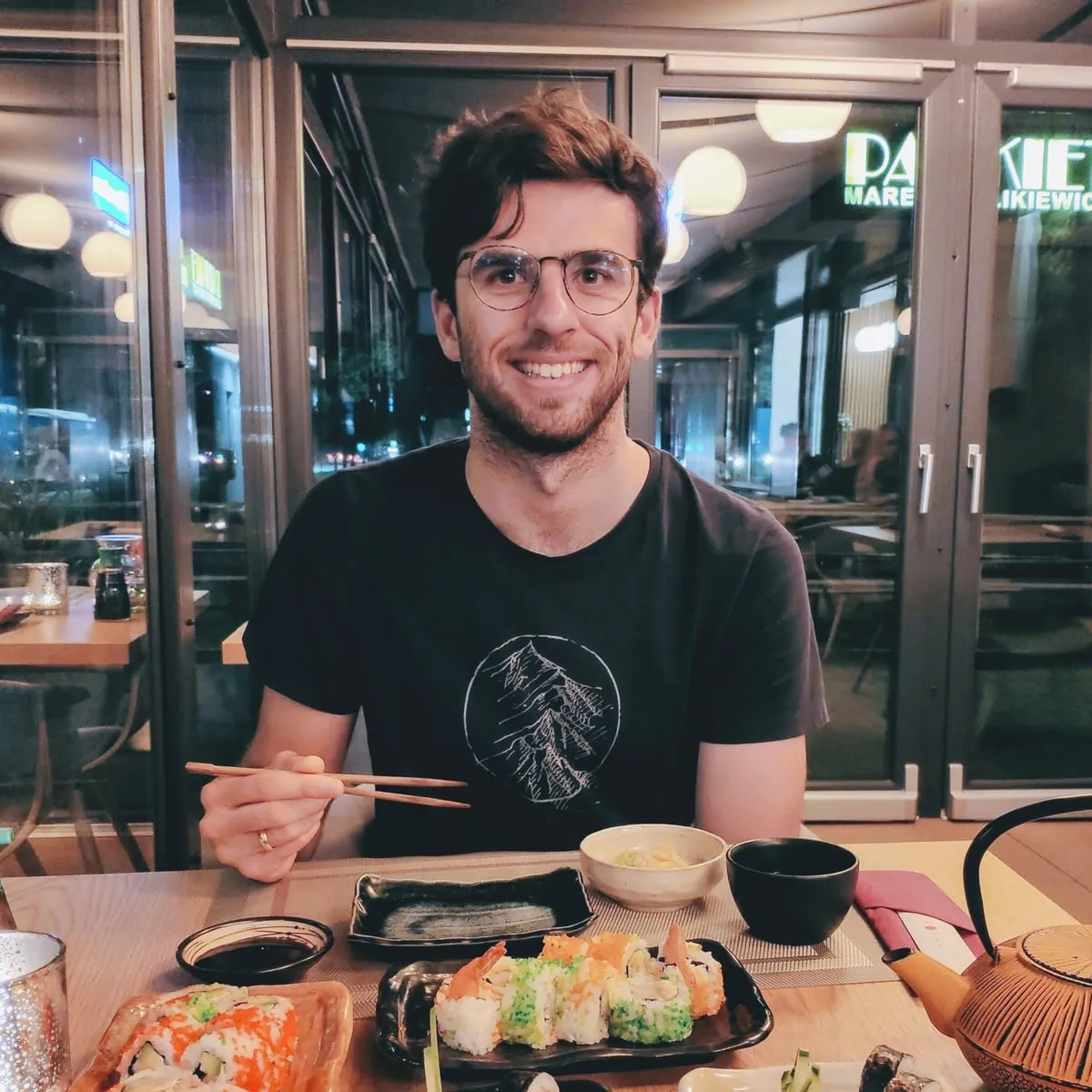 Konrad smiling at a restaurant table with sushi and chopsticks